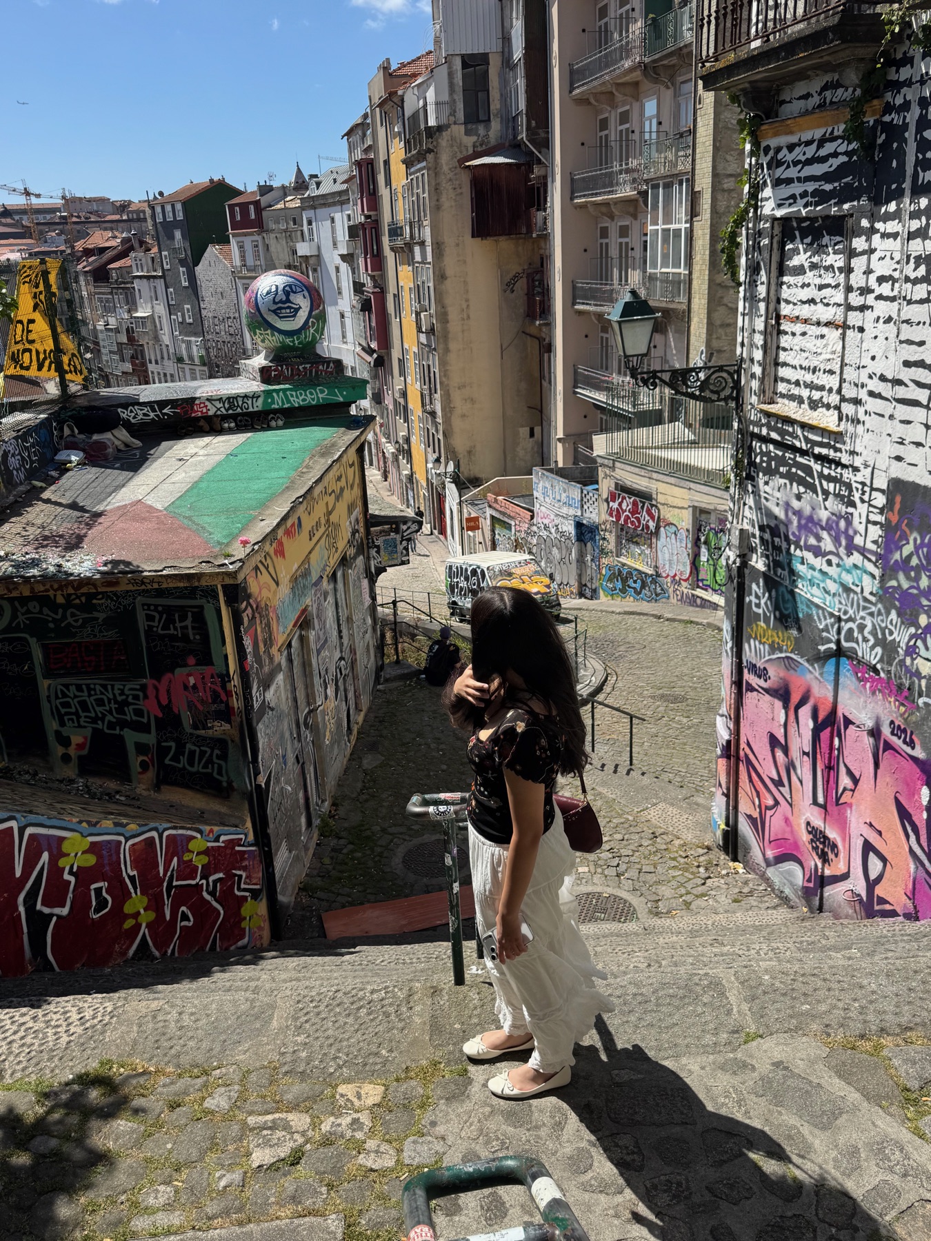 Datteren på en brostenstrappe mellem farverige graffitivægge i Porto.