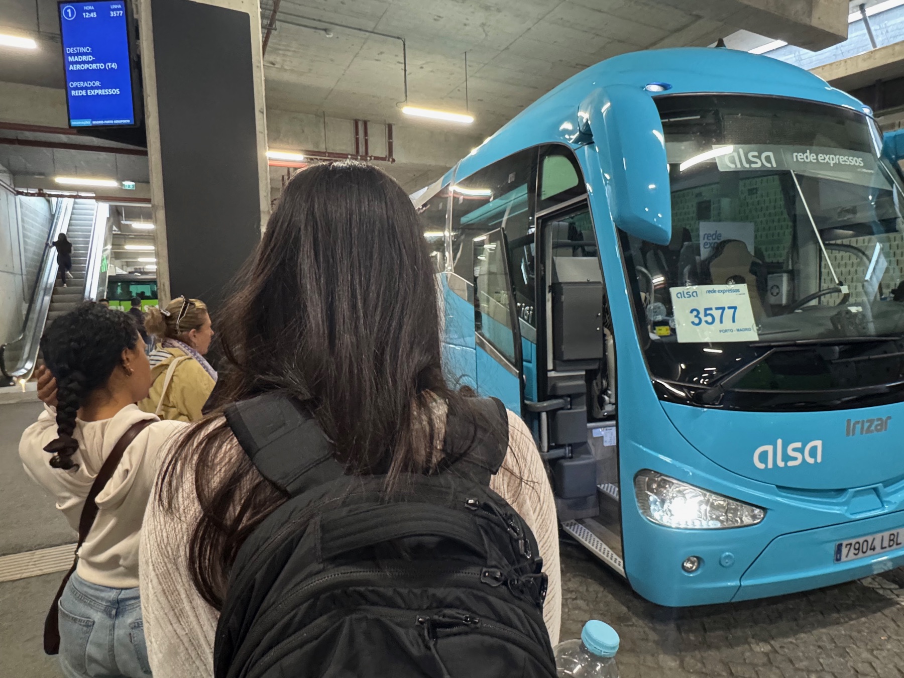 Datteren med rygsæk ved en stor blå bus med destination Madrid.